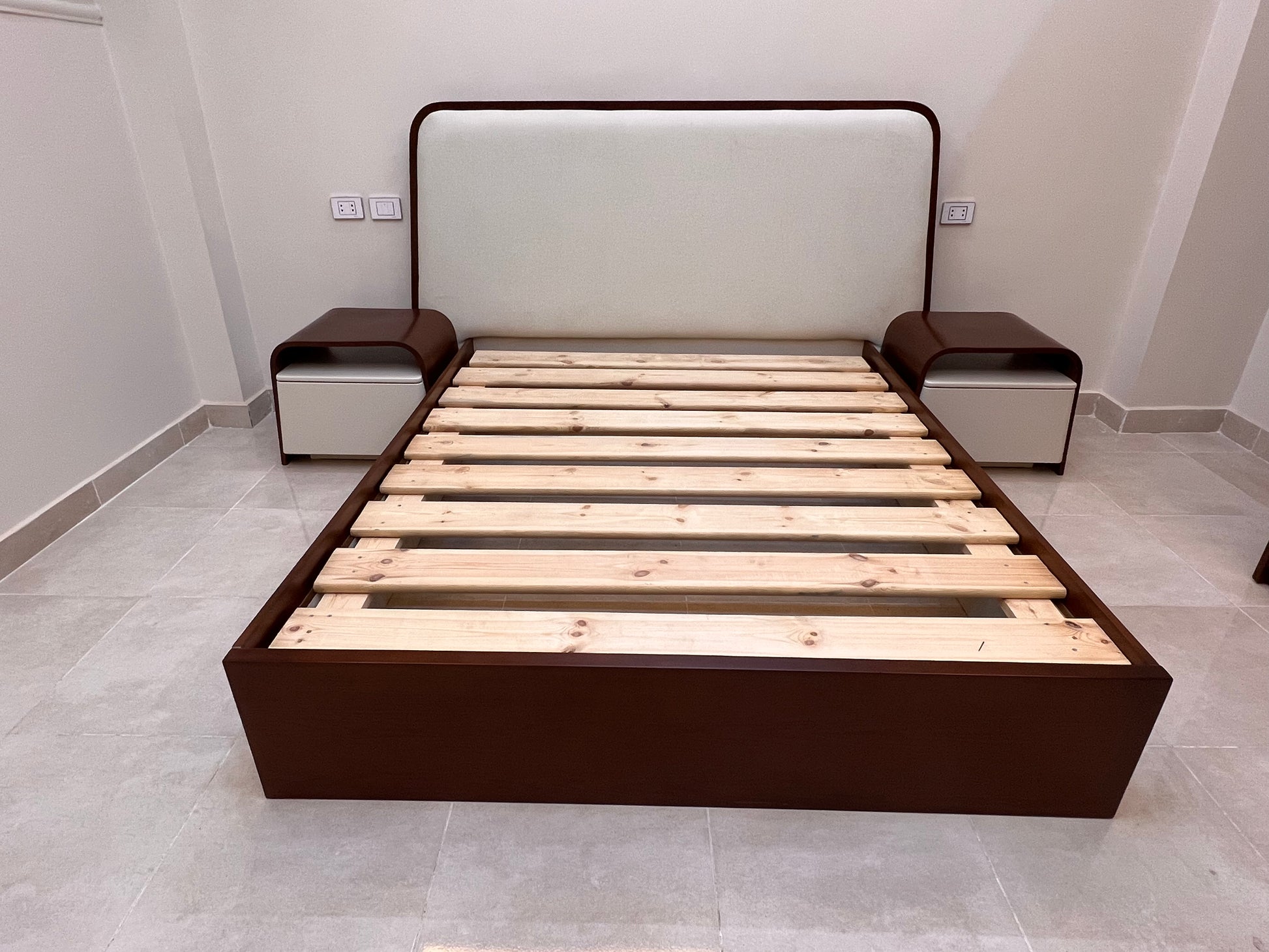 Wooden bed frame with dark brown frame and wooden slats on a tiled floor.