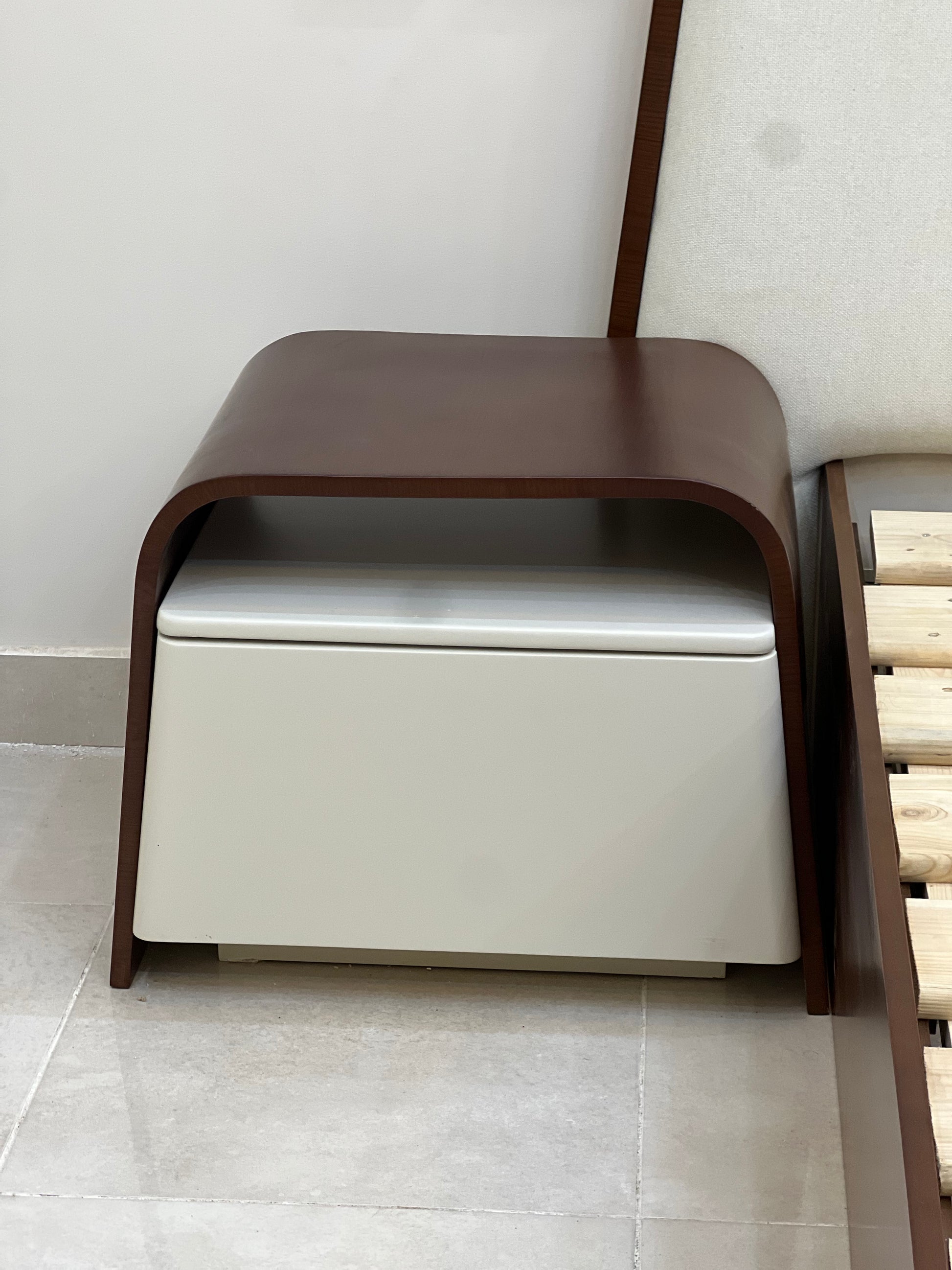 Modern ottoman with wooden frame and white cushion on a tiled floor.